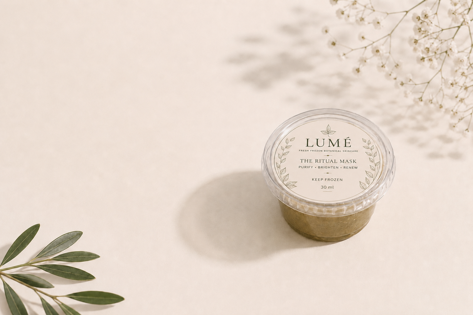 Approved LUMÉ hero photograph: a single LUMÉ Ritual Mask cup on a warm ivory surface with olive leaves and baby's breath
